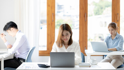 Startup company work atmosphere, female employee typing at the desk in company office, startup company operation by young generation. Concept of setting up and managing a startup company.