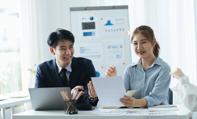 group of four happy young asian corporate people teammates meeting discussing business in office. Graphs on whiteboard behind them.