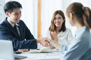 Group of beautiful designers in casual clothes is discussing affairs and smiling while working in studio. Two of them are shaking their hands