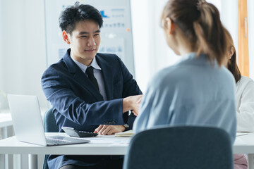 Group of beautiful designers in casual clothes is discussing affairs and smiling while working in studio. Two of them are shaking their hands
