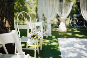 White chairs decorated by a bouquet of white flowers is preparing for the wedding.