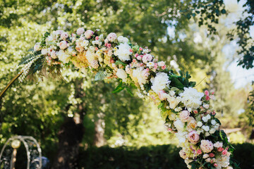 Details of the round wedding arch. Pink and white flowers, roses close-up, against a background of green trees in the park. 