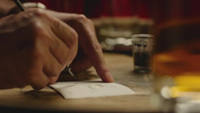 Closeup hand of man writing calligraphy with ink pen . Professional calligrapher painting , drawing on vintage paper . Beautiful handwriting . Poet writes letter , poem . Art of penmanship Slow motion