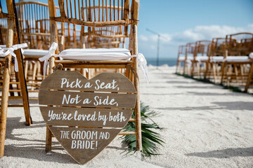 Pick A Seat Not a Side sign for the Wedding Ceremony Rows of wooden chairs for the wedding beach ceremony White sand background Cropped photo 