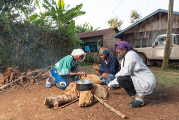 Older African Woman helping young teenage girls to  prepare a pot of tea