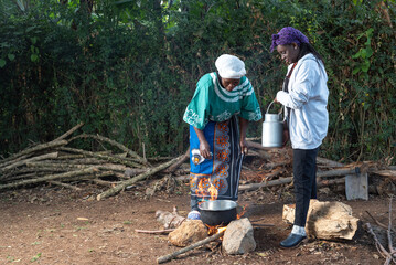 Older African Woman helping young teenage girls to  prepare a pot of tea