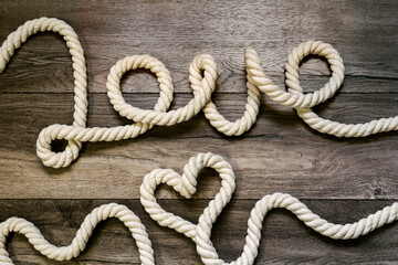 Inscription love and symbol heart made of rope on a wooden background