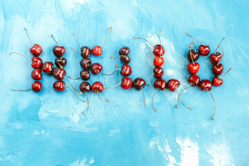 Lettering hello from ripe cherry fruits on a blue background