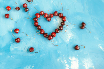 Heart shape made from ripe cherry fruits on a blue background
