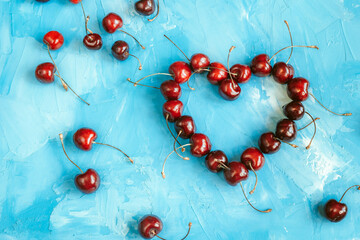 Heart shape made from ripe cherry fruits on a blue background