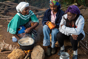Older African Woman helping young teenage girls to  prepare a pot of tea