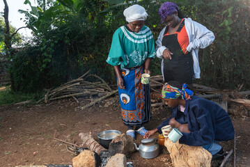Older African Woman helping young teenage girls to  prepare a pot of tea