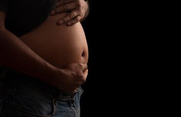 Close up man's tummy so big gesture like pregnant man on black background. Health care or Equality...