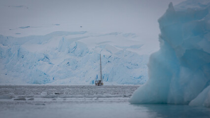 Ein einzelnes Segelschiff in einer eisigen Gletscherbucht bestehend aus blauem Gletschereis im...