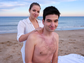 Male patient and therapist looking at the camera during an outdoors massage session on a beach in Valencia.