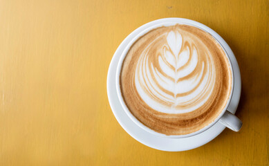 Top view of hot coffee with latte art on the yellow wooden background.