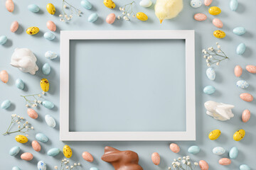Easter frame with sweet chocolate eggs and bunny, spring blossom flowers on blue background. Top view. Happy Easter greeting card with copy space.