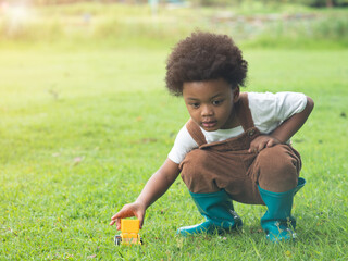 Cute little African boy wearing green gum boot playing with toy truck on the grass in the park