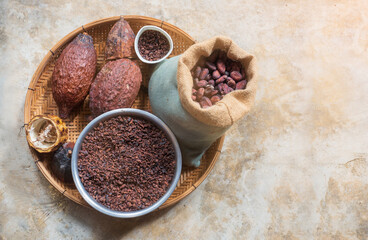 Top view, flat lay of cocoa beans in the sack, flakes, pods on the straw plate basket with copy space on the right.
