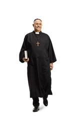 Full length portrait of a priest walking towards camera and holding a bible
