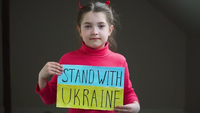 Portrait serious girl protesting armored conflict holding banner with inscription Stand with Ukraine at blue yellow flag. Crisis, peace, stop aggression in whole world