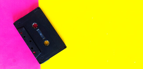 Retro 80-s or 90-s concept. Black Audio cassette on a pink yellow creative background, top view.