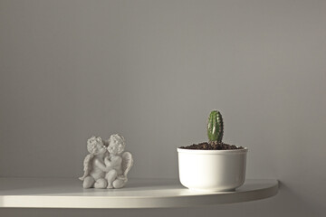 Cactus in white pot and statue angels on white shelf