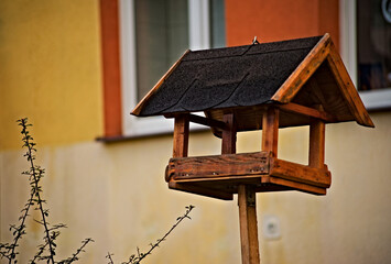 Drewniany karmnik dla ptaków wykonany ręcznie , ustawiony przed budynkiem z oknem . 