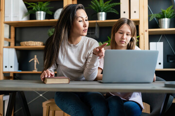 Happy young asian single mother studying with teenage child girl using laptop at home schooling