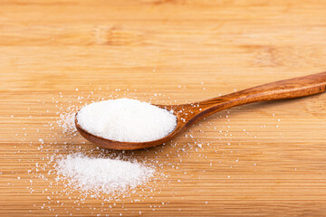 Wooden spoon with white sugar on a wooden background.