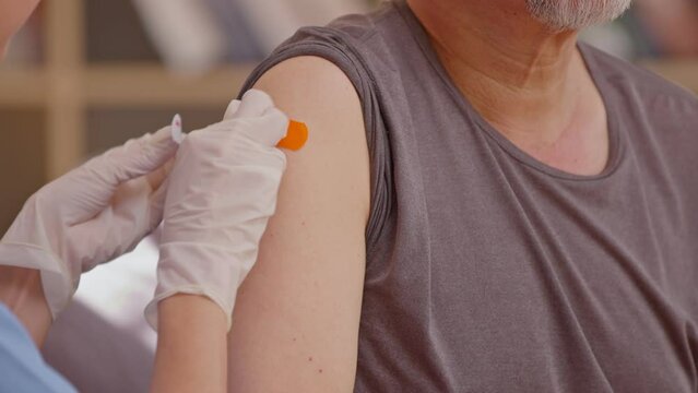 Asian old man got vaccine injection with a syringe needle for an elderly Senior patient. Doctor wearing white gloves and put band aid on his shoulder.