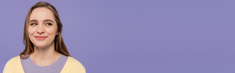 sly young woman looking away and smiling isolated on purple, banner.