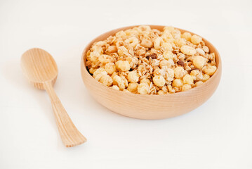 Dry muesli with cornflakes, nuts and raisins in a wooden bowl on a white background