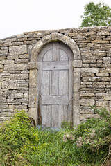 Fototapeta na wymiar A rather curious door in a dry stone wall leading into a perfectly ordinary field near the Cotswold village of Dowdeswell, Gloucestershire, England UK