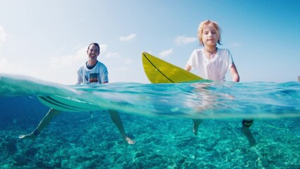 Boy surfs with his father. Preteen boy sits on the surf board in the tropical ocean with his family