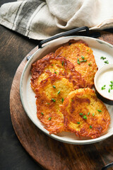Potato pancakes. Fried homemade potato pancakes or latkes with cream and green onions in rustic plate on old wooden black table background. Rustic style. Healthy food. Top view.