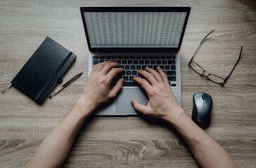 Workspace on the table. Hands typing on a laptop keyboard. Black notebook, glasses, pen, computer...