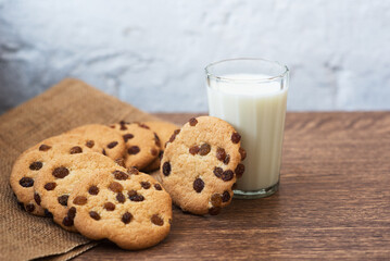 Fragrant, tasty, homemade cookies in nonwoven brown fabric with raisins and a glass of fresh milk on the table. Delicious, hearty, healthy breakfast. Copy space, high resolution