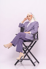 Close up portrait of businesswoman wearing stylish light purple office attire with hijab, sitting on a director chair isolated over white background. Fashion, beauty, corporate, lifestyle concept. 