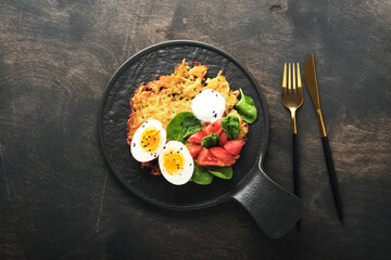Potatoes latkes with sour cream, spinach salad, tomatoes and boiled eggs on dark wooden old table background. Homemade tasty potato pancakes. Delicious food for breakfast. Top view.