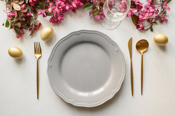Easter table setting with golden eggs and cutlery, gray plate on white background. Top view....
