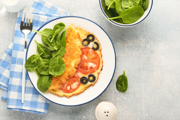 Omelette with tomatoes, black olives, cottage cheese and green spinach herbs on white plate on grey concrete background. Delicious breakfast. Healthy breakfast food. Top view.