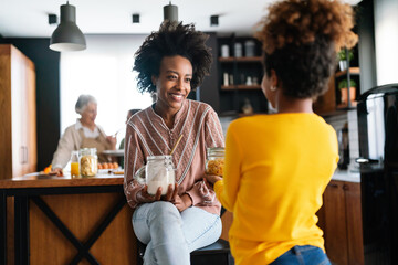 Cute african american teen girl with mother having pleasure conversation and smiling in kitchen