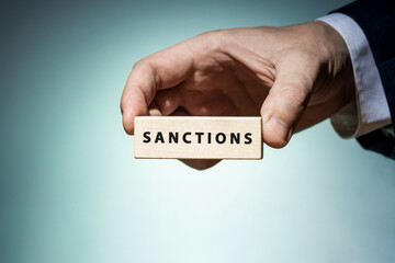 businessman hold wooden block with word Sanctions inscription over blue background. studio shot. sanction to russia illustrative concept