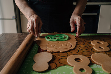  Grandmother makes gingerbread cookies with her hands and cuts out figure eights for March 8. Baking equipment. Home cooking handmade. High quality photo