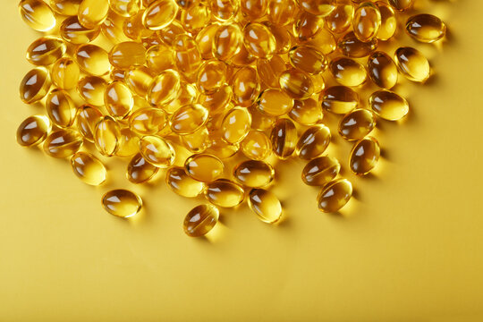 Pile of golden capsules of vitamin D3 on a yellow background with free space