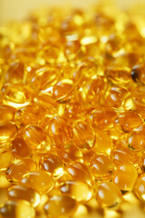 Pile of golden capsules of vitamin D3 on a yellow background with free space