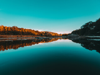 Sonnenuntergang im Wald über dem See. Blaues Wasser und kühle Spiegelung des Himmels. Das saubere Wasser