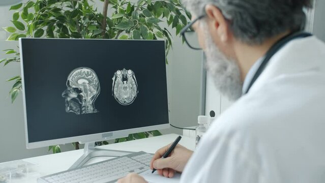 Mature doctor working with computer analyzing brain scan on screen indoors in hospital office. Modern technology and medicine concept.