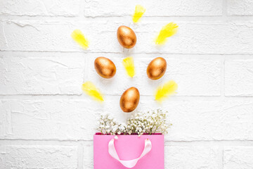 Obraz na płótnie Canvas Paper pink eco-bag with golden Easter eggs and yellow feathers on a white brick background. Banner for a happy Easter holiday. Flat position, top view. The concept of discounts and sales